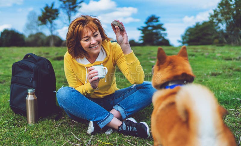 Happy girl with smile drink cup playing with red japanese dog shiba inu on green grass in the outdoors nature park stock photo Happy girl with smile drink cup playing with red japanese dog shiba inu on green grass in the outdoors nature park stock photo