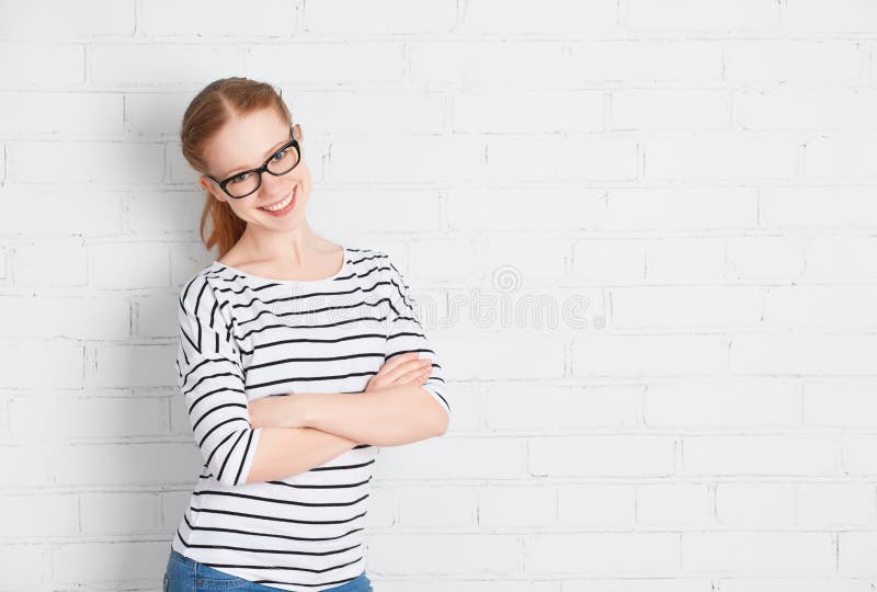 Happy girl student in glasses at a blank white brick wall