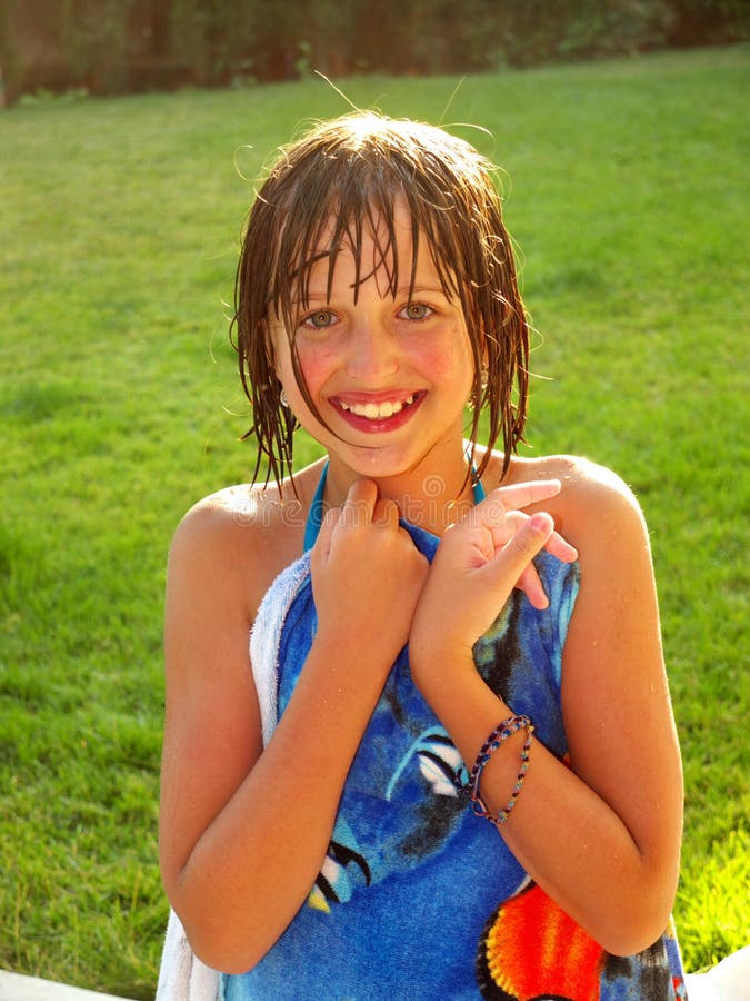 Wet girl just out of the pool, in swimsuit holding a blue towel. Blond hair and smiling face. Green grass in the background. Wet girl just out of the pool, in swimsuit holding a blue towel. Blond hair and smiling face. Green grass in the background