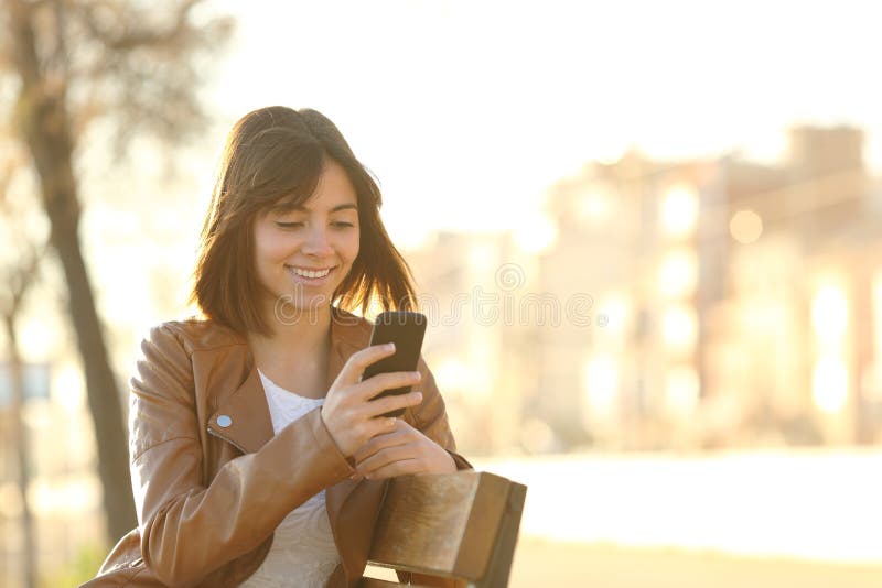 Happy girl using a smart phone in a city park