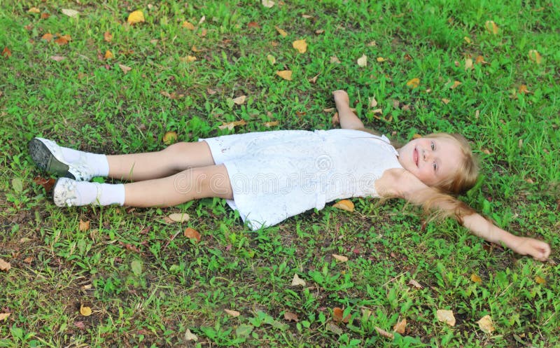 Happy girl in white lies on green grass in summer park