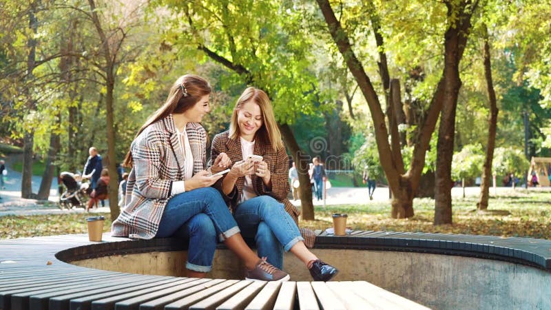 Happy Girls, die über Smartphones im öffentlichen Park in sozialen Medien surfen