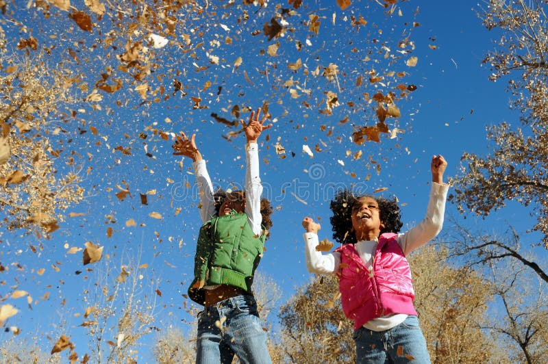 A picture of jovial girls playing in a park, jumping and throwing dry leaves in the air. A picture of jovial girls playing in a park, jumping and throwing dry leaves in the air.