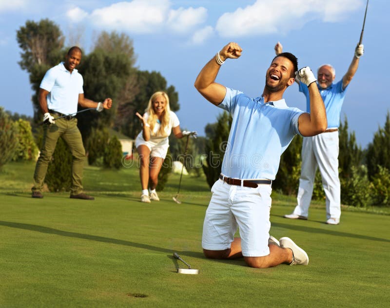 Felice per il golfista in ginocchio al foro sollevato i pugni dopo aver messo in con la palla da golf in buca.