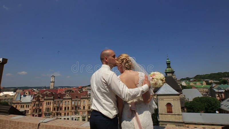 Happy gorgeous bride and stylish groom with true emotions on the roof on background of view of old city buildings