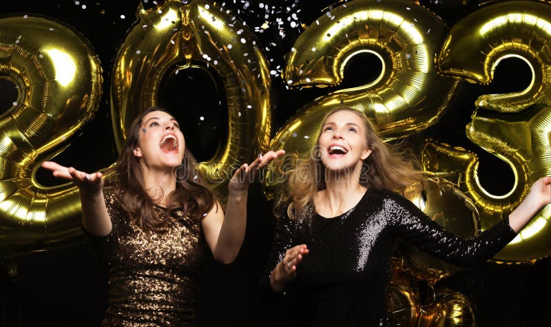 Happy gorgeous girls in stylish sexy party dresses holding gold 2023 balloons, having fun at New Year& x27;s Eve Party.