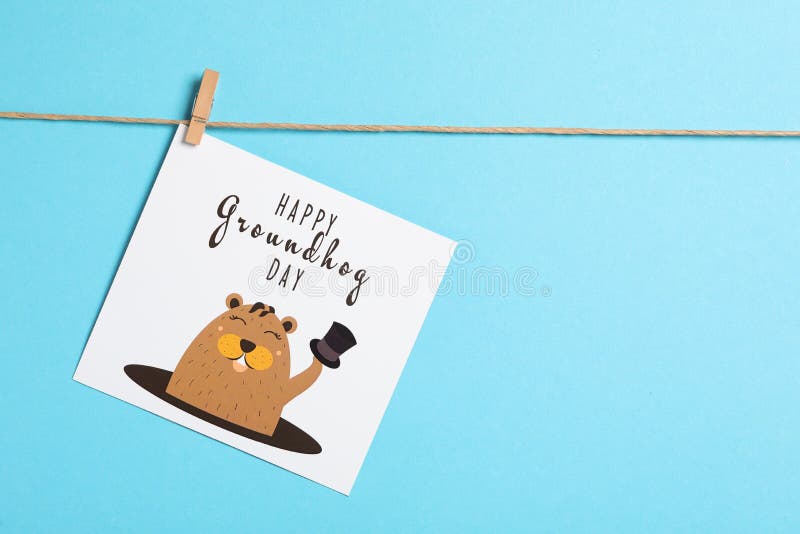 Happy Groundhog Day greeting card hanging on light blue background, space for text