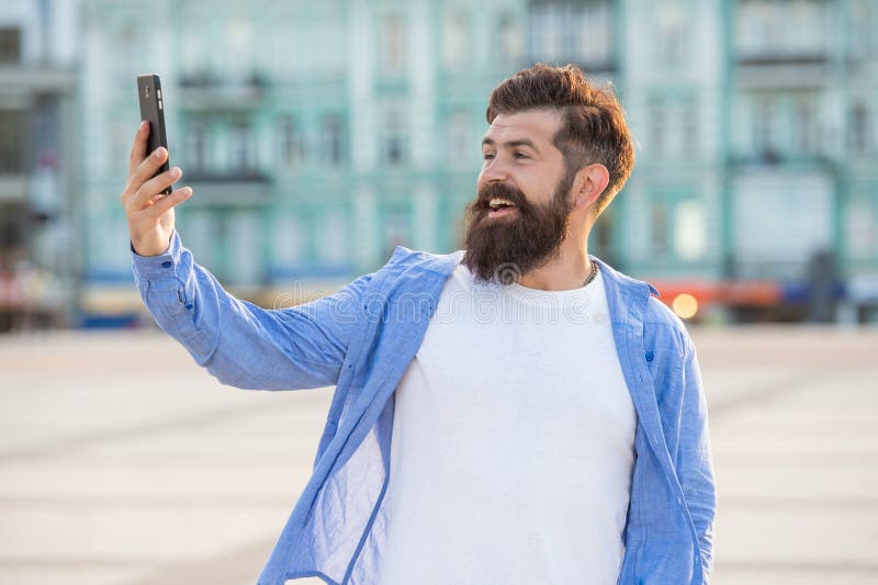 Happy guy making video call through mobile Internet outdoors. Bearded guy smiling to smartphone royalty free stock photography