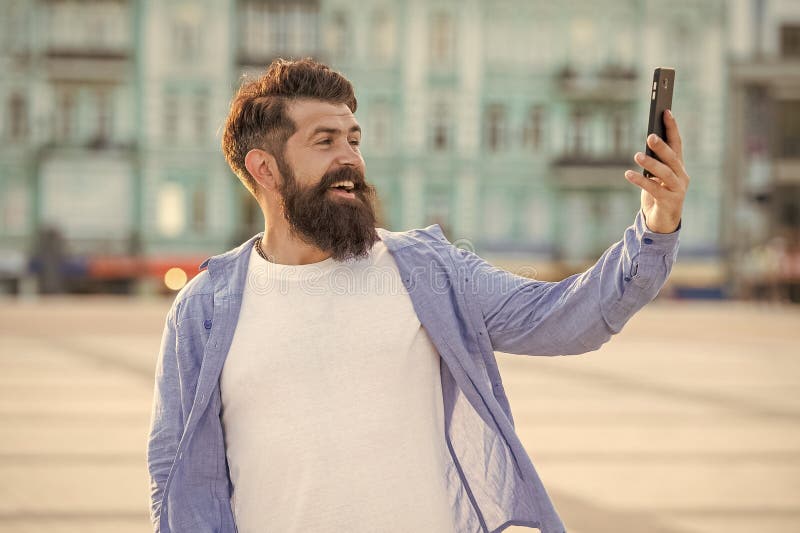 Happy guy making video call through mobile Internet outdoors. Bearded guy smiling to smartphone royalty free stock photo