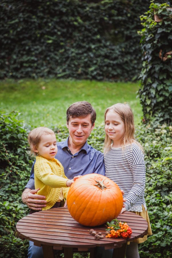 Happy halloween. Father and two daughters look at the face cut in the pumpkin for Halloween outside. stock photos Happy halloween. Father and two daughters look at the face cut in the pumpkin for Halloween outside. stock photos