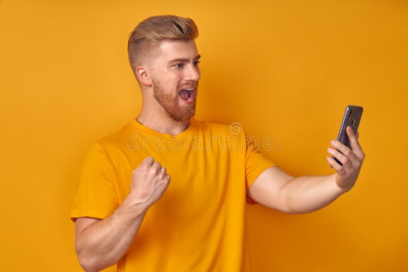 Happy handsome red beard caucasian man stand on orange studio background hold smartphone feel excited get pleasant stock image Happy handsome red beard caucasian man stand on orange studio background hold smartphone feel excited get pleasant stock image