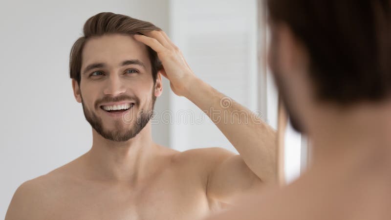 Happy handsome young guy combing smooth brown hair with fingers