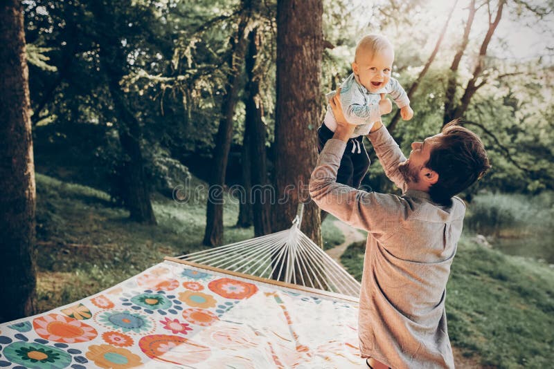 Happy hipster father playing with his son in a park near a hammock while on camping trip in the woods, family concept, handsome