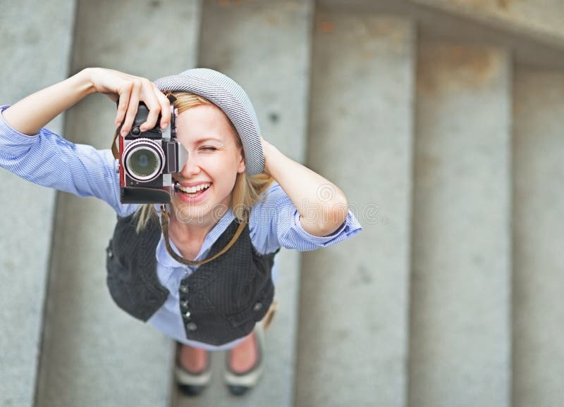 Felice hipster ragazza in cappello di fare foto con la fotocamera retrò su strada di città.