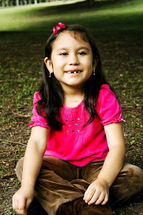 Happy hispanic girl sitting on the grass.