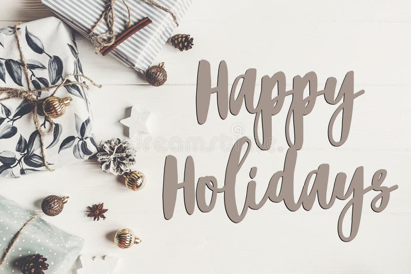 Happy holidays text, seasonal greetings card sign. stylish mode. Rn presents with ornaments cones anise on rustic white wooden background top view. xmas flat lay stock images Happy holidays text, seasonal greetings card sign. stylish mode. Rn presents with ornaments cones anise on rustic white wooden background top view. xmas flat lay stock images
