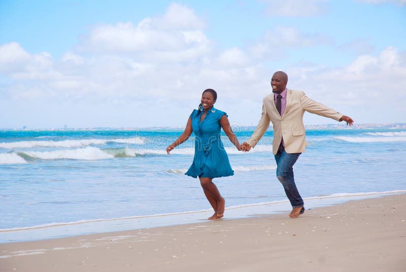 Ein Afroamerikaner schwarze paar mit glücklich lächelnden Gesichtsausdruck laufen zusammen hand in hand am Strand am Tag der Flitterwochen Ankunft.