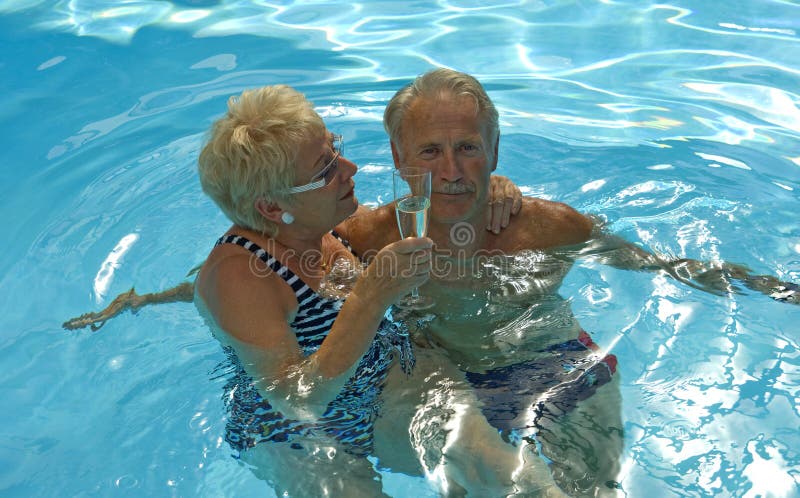 Rádi starší manželský pár se baví, zatímco pití šumivého vína v modré vodě bazénu na na krásný den v létě.