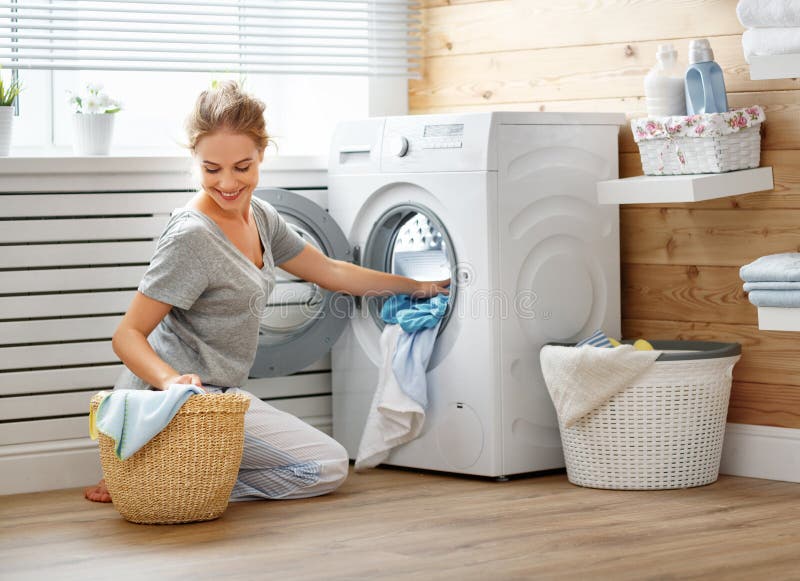 Happy housewife woman in laundry room with washing machine stock images