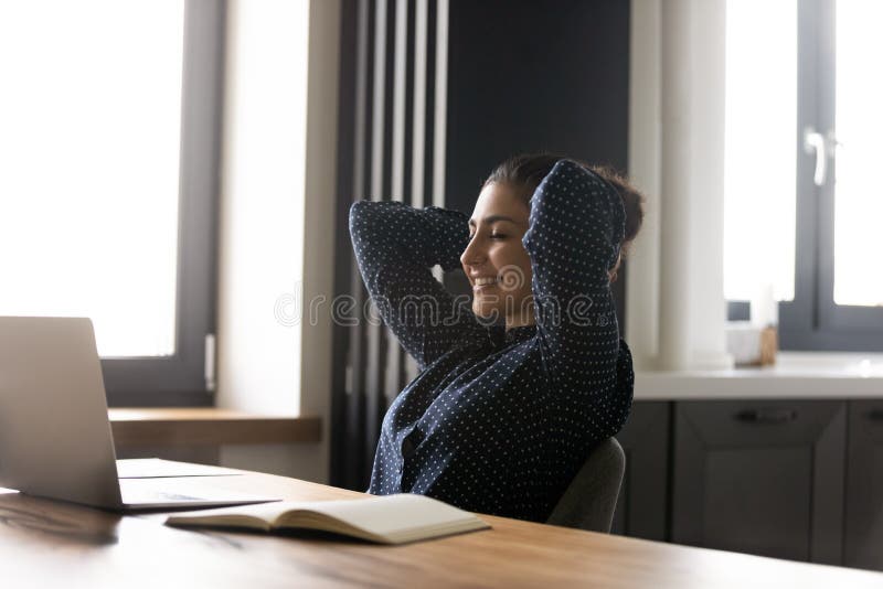 Happy Indian woman relax at workplace distracted from computer work