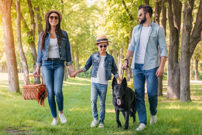 Young happy interracial family with picnic basket walking with dog in forest