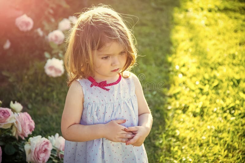 Happy kid having fun. Child with thinking face in blue dress at blossoming roses