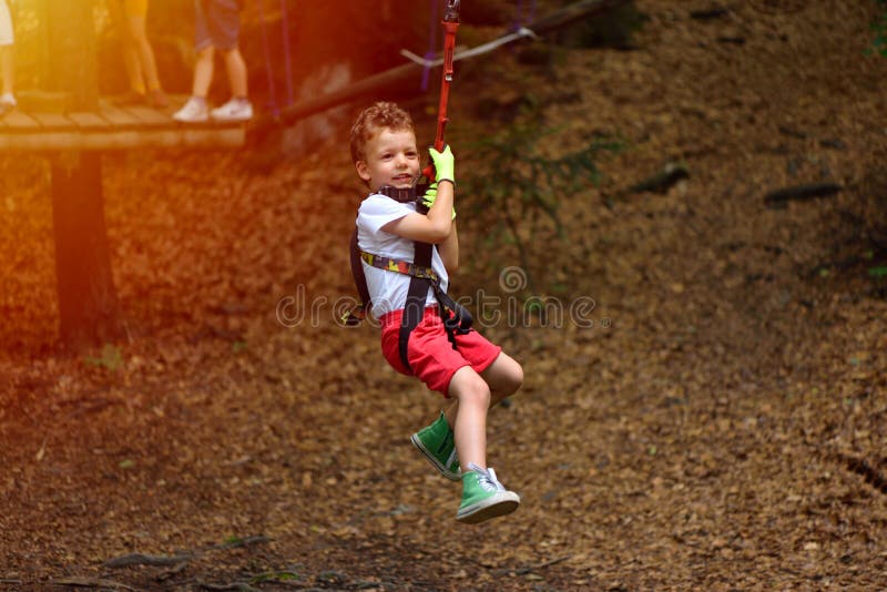 Happy kid with helmet and harness on zip line between trees stock photos Happy kid with helmet and harness on zip line between trees stock photos