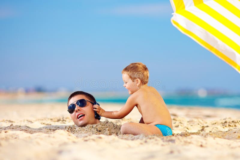 Happy kid helping father talk on the phone in sand