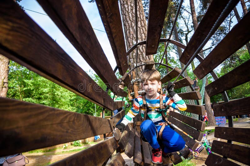 Happy kid overcomes obstacles in rope adventure park. Summer holidays concept. Little boy playing at rope adventure park. Modern stock images Happy kid overcomes obstacles in rope adventure park. Summer holidays concept. Little boy playing at rope adventure park. Modern stock images