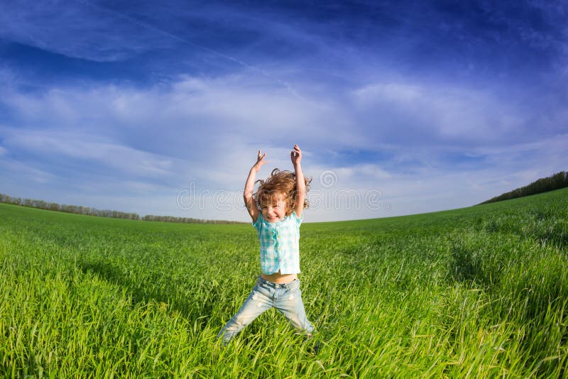 Happy kid with raised arms in green spring field against blue sky. Freedom and happiness concept