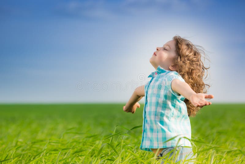 Happy kid with raised arms in green spring field against blue sky. Freedom and happiness concept