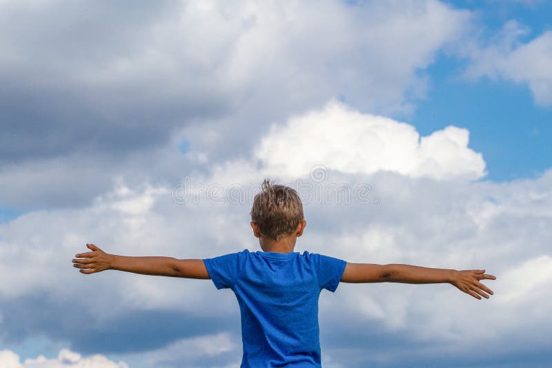 Happy kid with raised arms against blue sky. Freedom, joy and happiness concept.