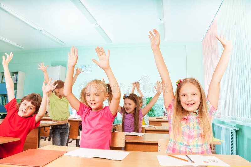 Happy kids with arms up sit in classroom rows royalty free stock images