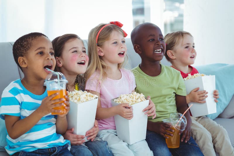 Happy kids enjoying popcorn and drinks while sitting stock image Happy kids enjoying popcorn and drinks while sitting stock image