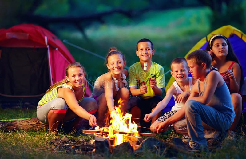 Group of happy kids roasting marshmallows on campfire