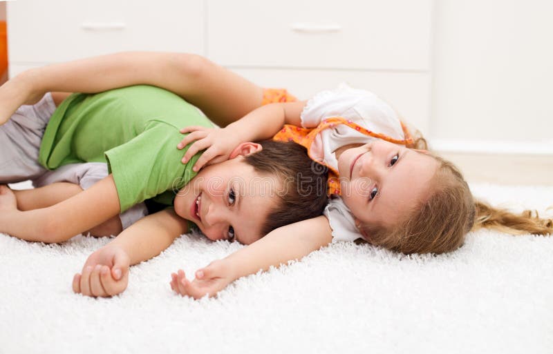 Happy kids boy and girl wrestling in their room laying on the floor - focus on the girl. Happy kids boy and girl wrestling in their room laying on the floor - focus on the girl