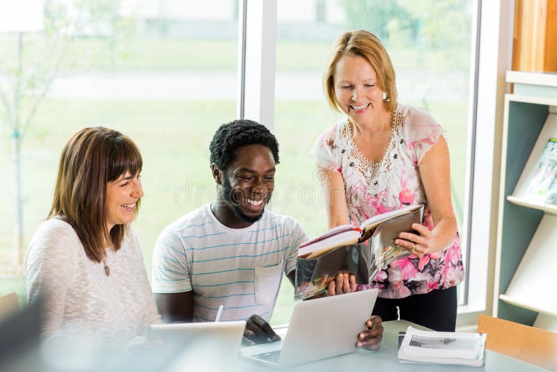 Happy Librarian Assisting Students In Library stock photo Happy Librarian Assisting Students In Library stock photo