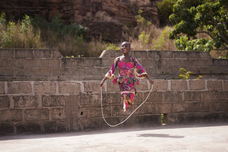 Happy Little African Girl Playing Outdoor With Her Skipping Rope, candid photo of real African children in a natural village environment