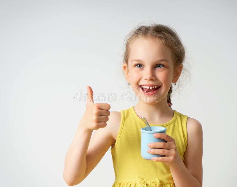 Happy little blonde girl in yellow clothing is delighted with tasty food showing shiny smile and thumb up gesture. Close stock photo Happy little blonde girl in yellow clothing is delighted with tasty food showing shiny smile and thumb up gesture. Close stock photo