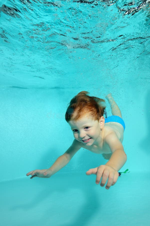Happy little boy dives underwater to the bottom of the pool on a blue background and smiles. stock photo Happy little boy dives underwater to the bottom of the pool on a blue background and smiles. stock photo