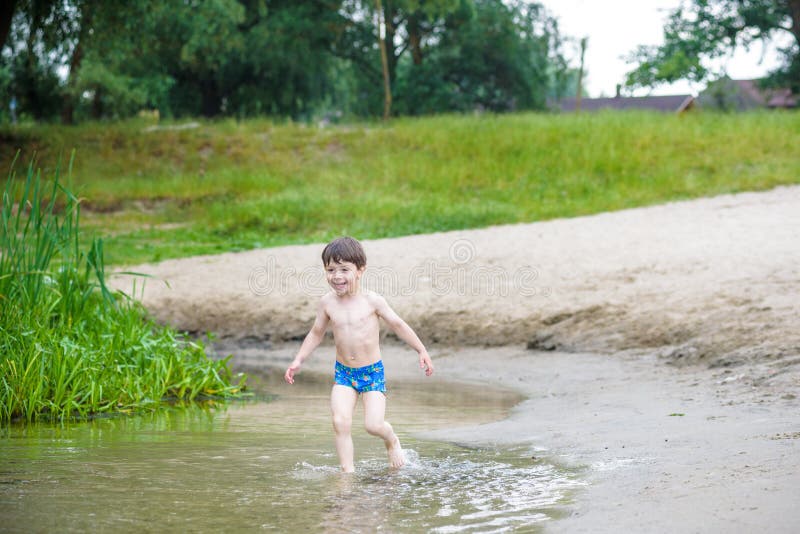 Happy little boy having fun and running in water in the river at summer day time, summertime lifestyle outdoor, friendly family we