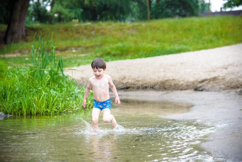 Happy little boy having fun and running in water in the river at summer day time, summertime lifestyle outdoor, friendly family we