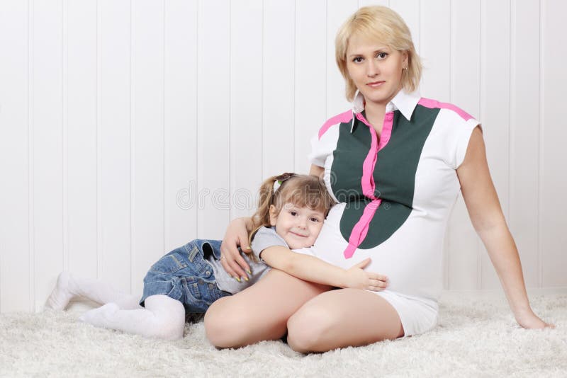 Happy little daughter lies on carpet and hugs belly