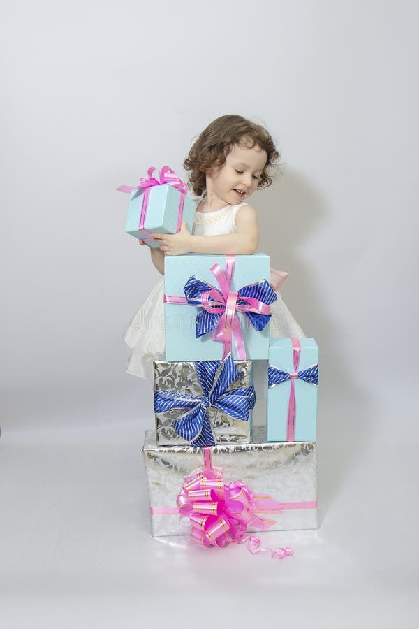 Happy little girl, adorable toddler in a white dress, holding many birthday or christmas presents, opening boxes decorated with royalty free stock images Happy little girl, adorable toddler in a white dress, holding many birthday or christmas presents, opening boxes decorated with royalty free stock images