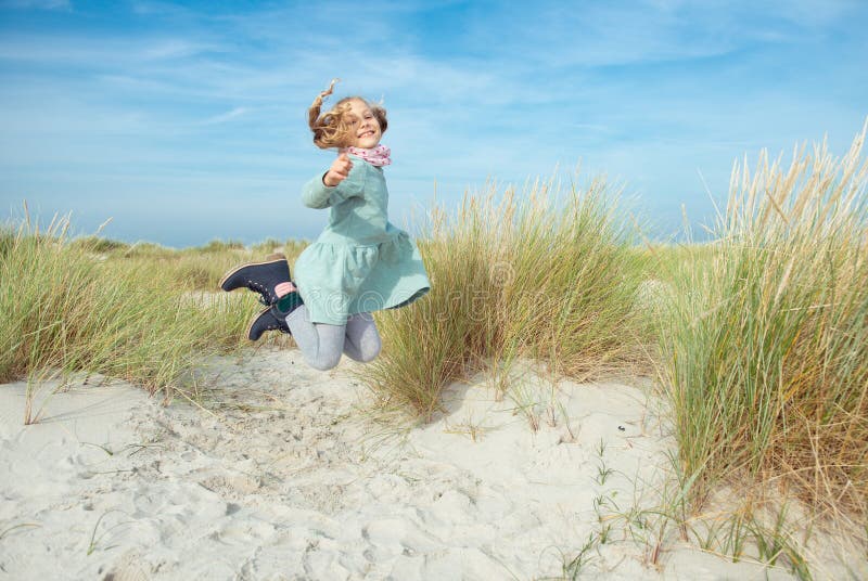 Happy little girl in blue dress jumping on beach at sunny day