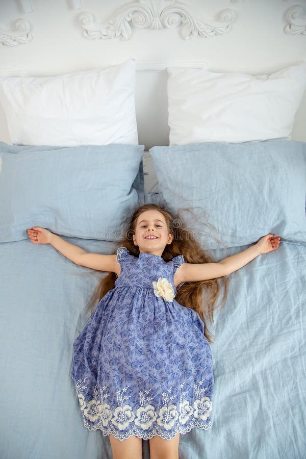 Happy little girl in a bright room is lying on the bed