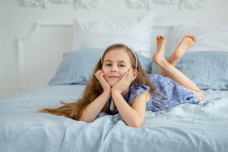 Happy little girl in a bright room is lying on the bed