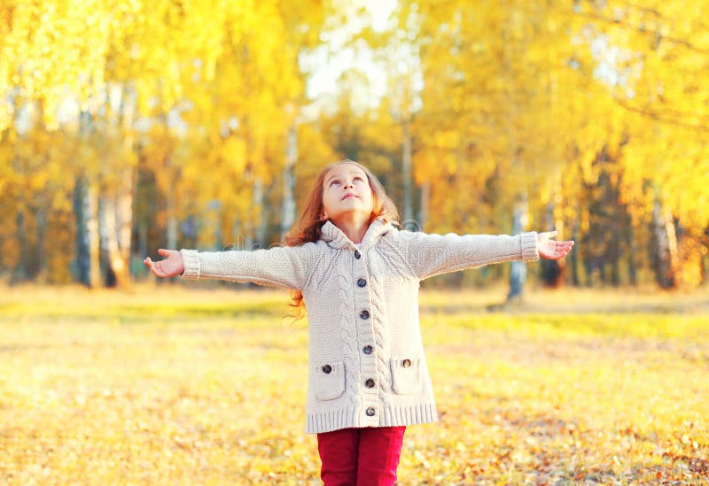 Happy little girl child enjoys warm sunny autumn day looks up walks in park