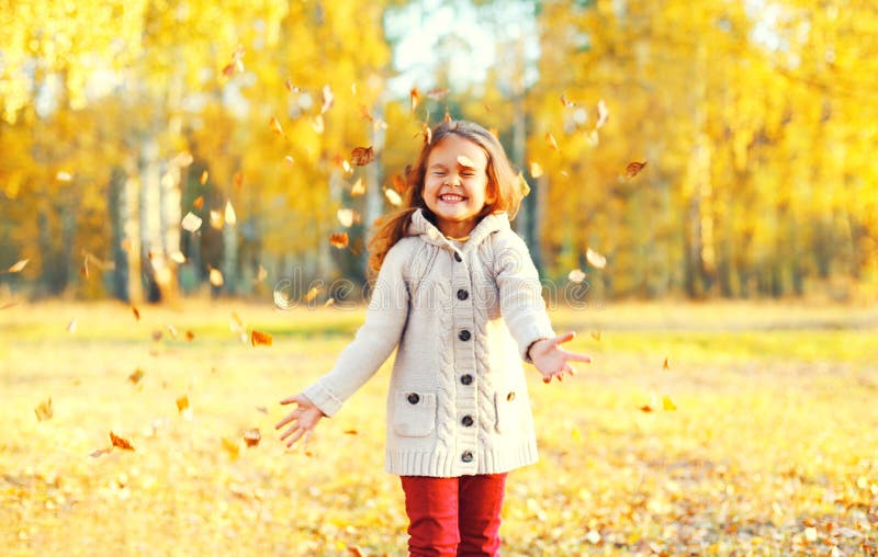 Happy little girl child having fun playing with yellow leafs in sunny autumn