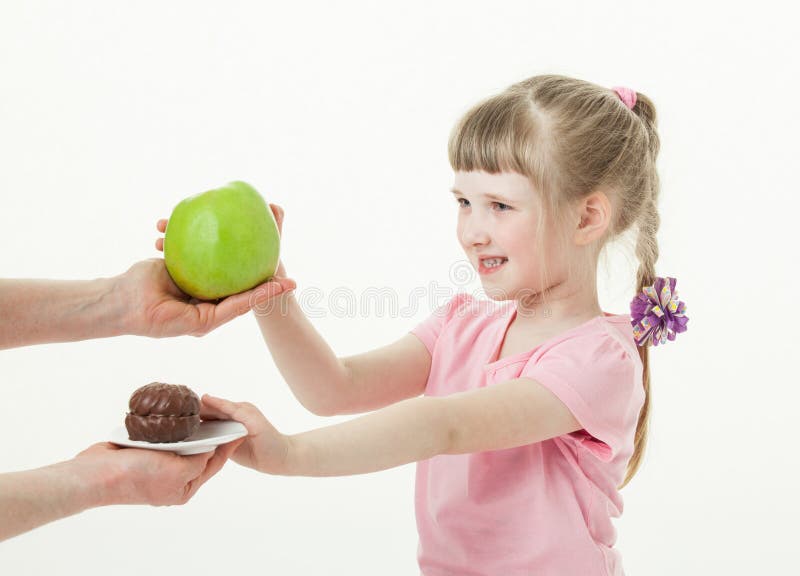 Happy little girl choosing a green apple and refusing a cake